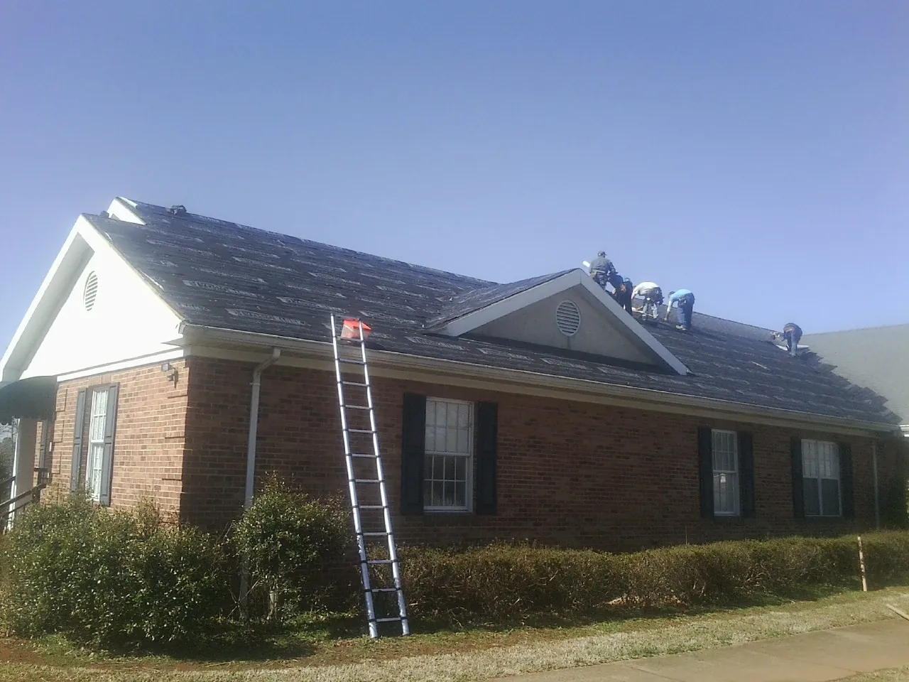 Crew tearing shingles off a brick ranch roof with a ladder set — Emergency Roof Repair work by our crew in Olalla
