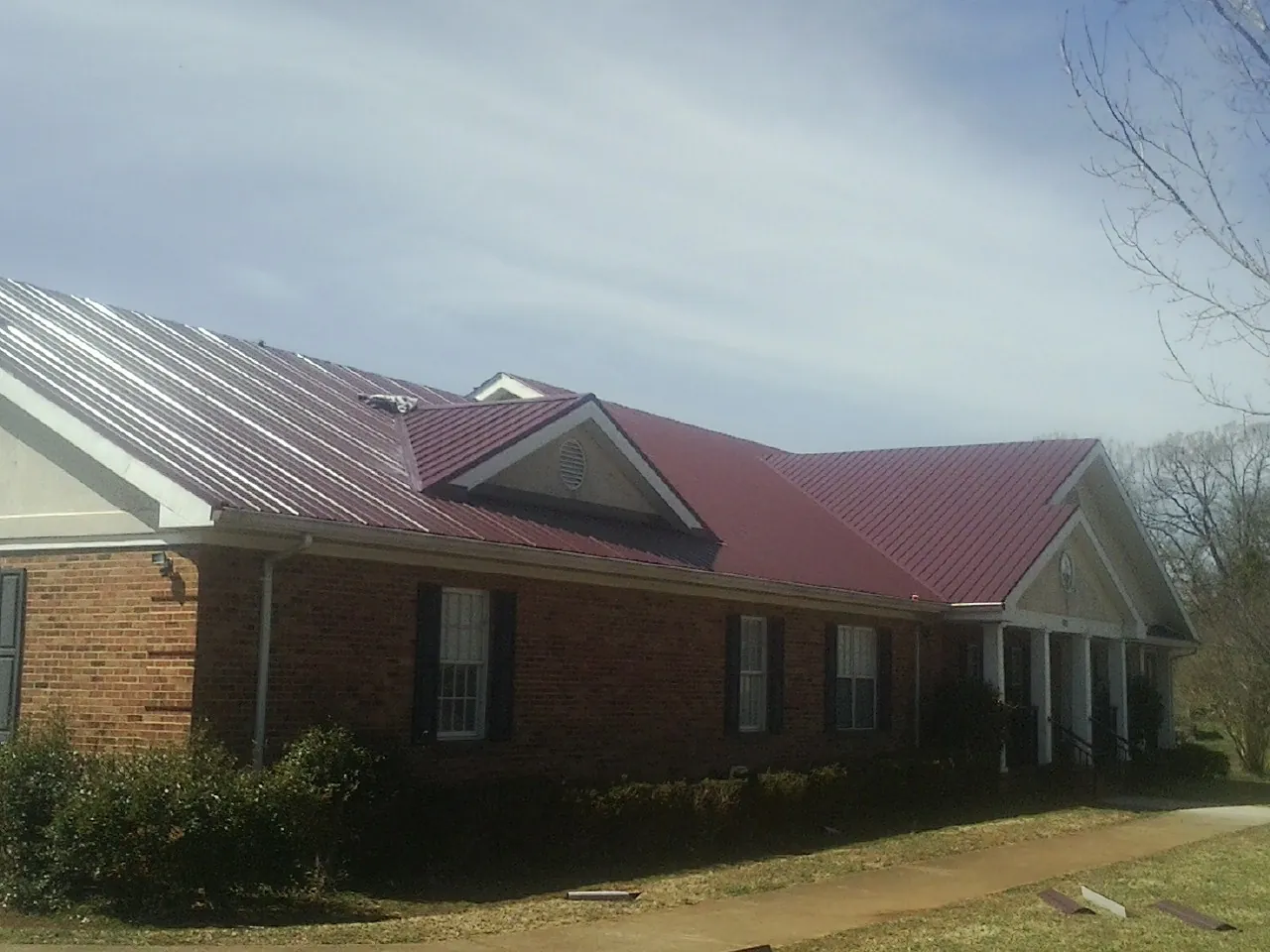 Red metal roof with gabled entries on a long brick building, from a Hail Damage Roof Repair job in Olalla