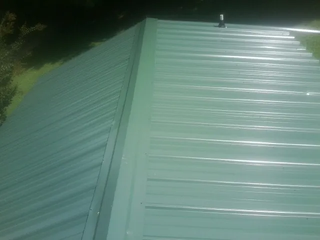 New green metal panels meeting at the ridge of a roof — Flat Roof Repair work by our crew in Olalla