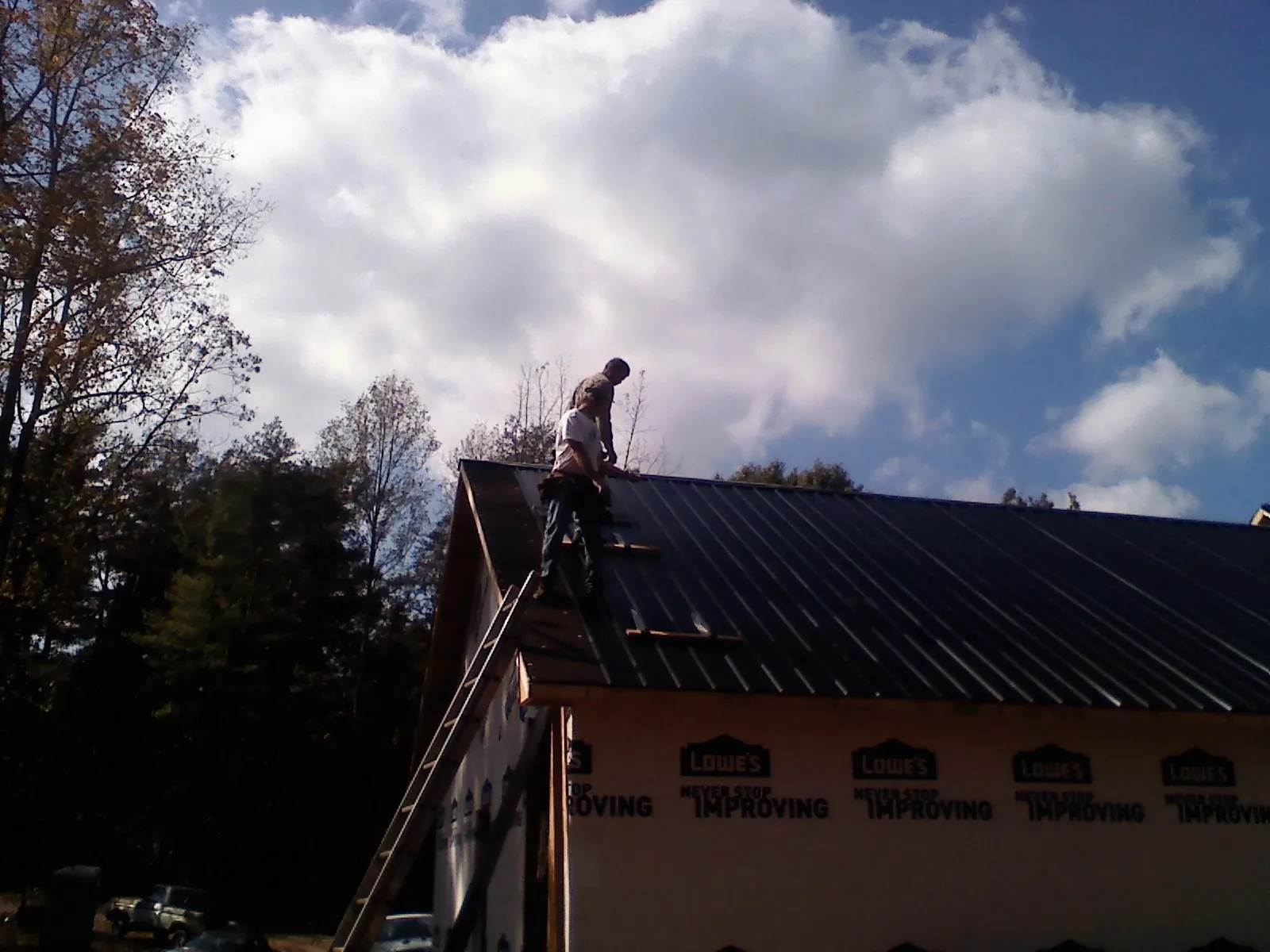 Roofer fastening dark metal panels high against a cloudy sky, from a Roof Inspection job in Olalla